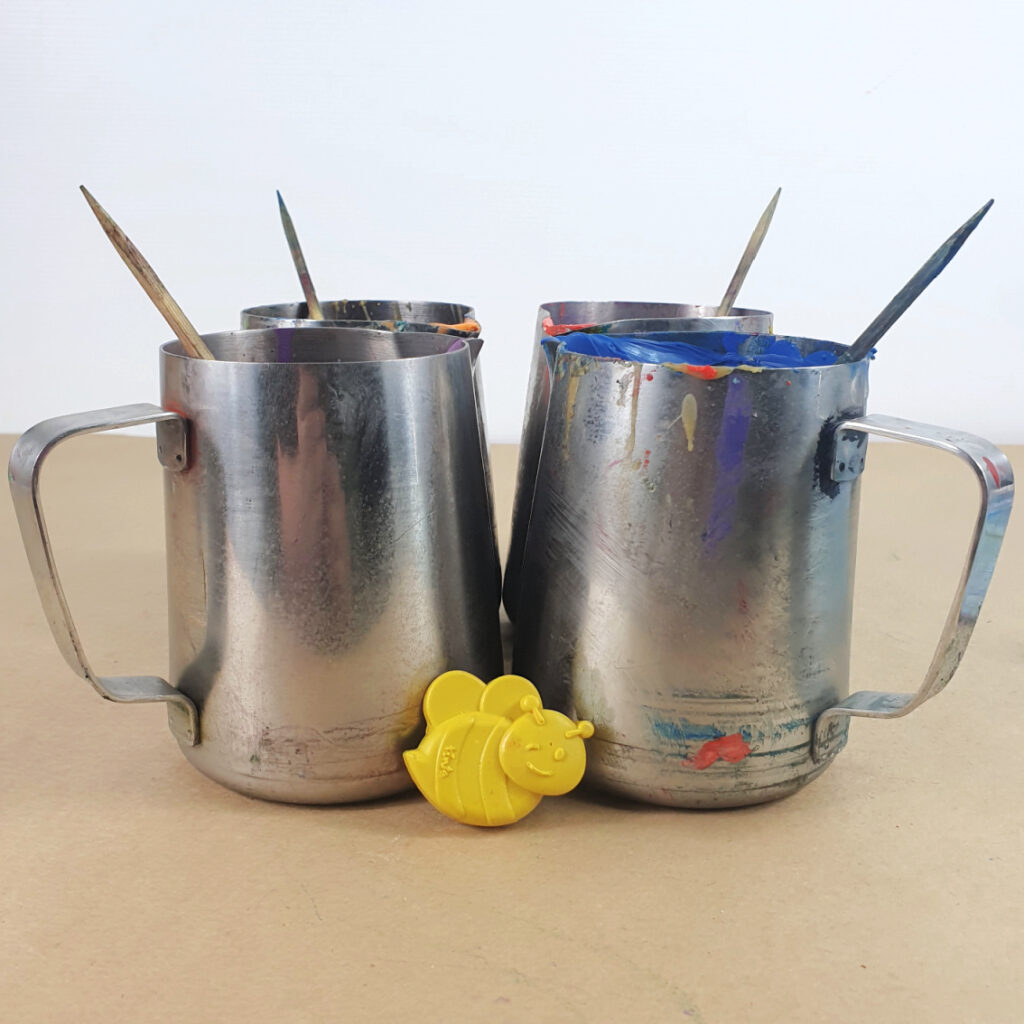 Four small pouring pots stand with a bee crayon for scale